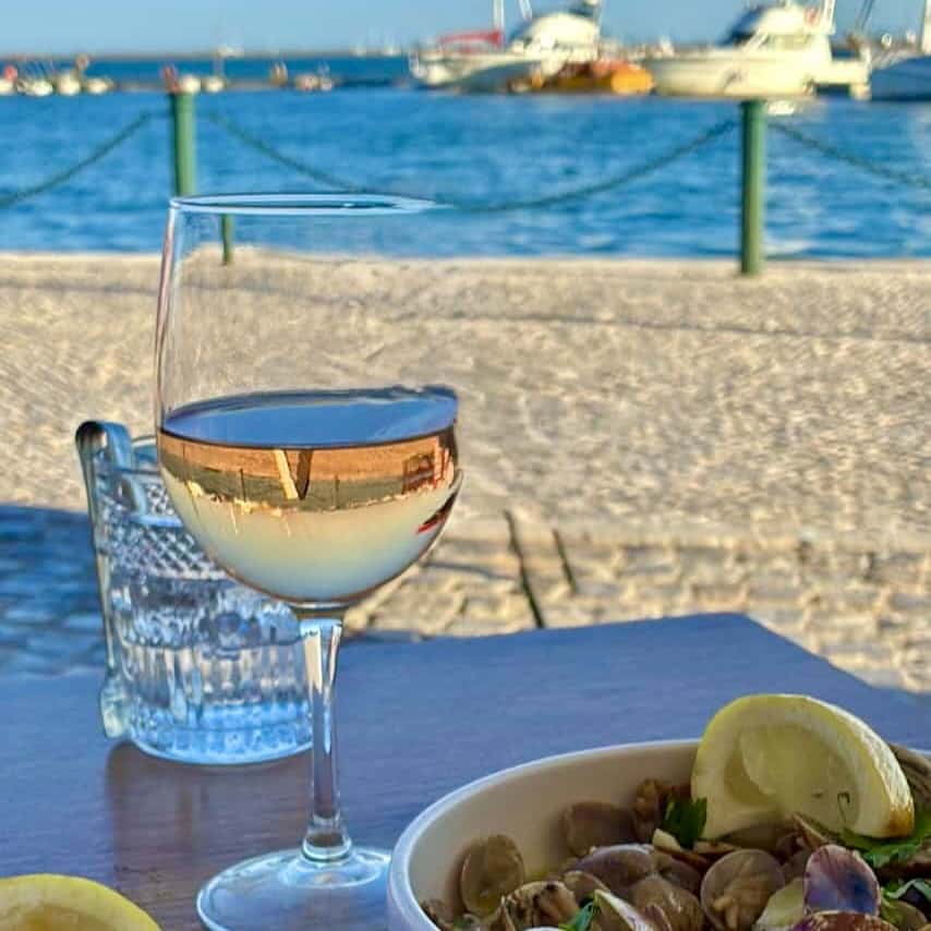 Glas of wine and bowl of amejoas on a table at the seaside with boats in the background