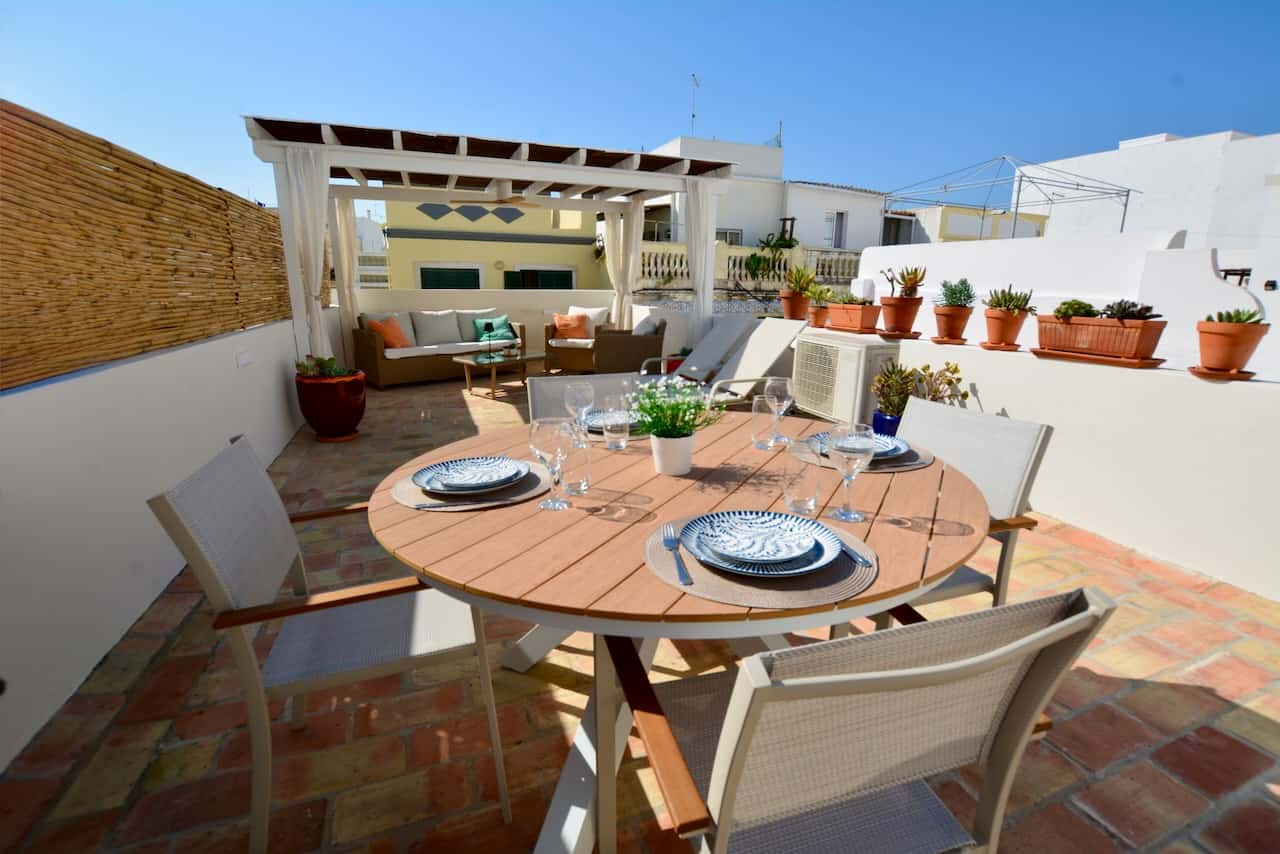 Dakterras met gedekte tafel en loungeset achterin; traditionele Santa Catarina-tegels tegen een helderblauwe hemel in de Algarve