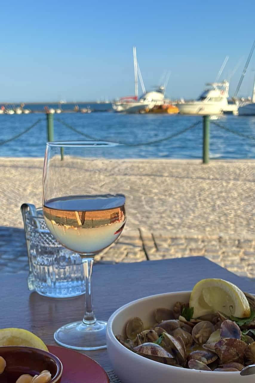 Tafelt bij een restaurant aan de haven van Olhão met een glas witte wijn en een schaaltje venusschelpen (amejoas)